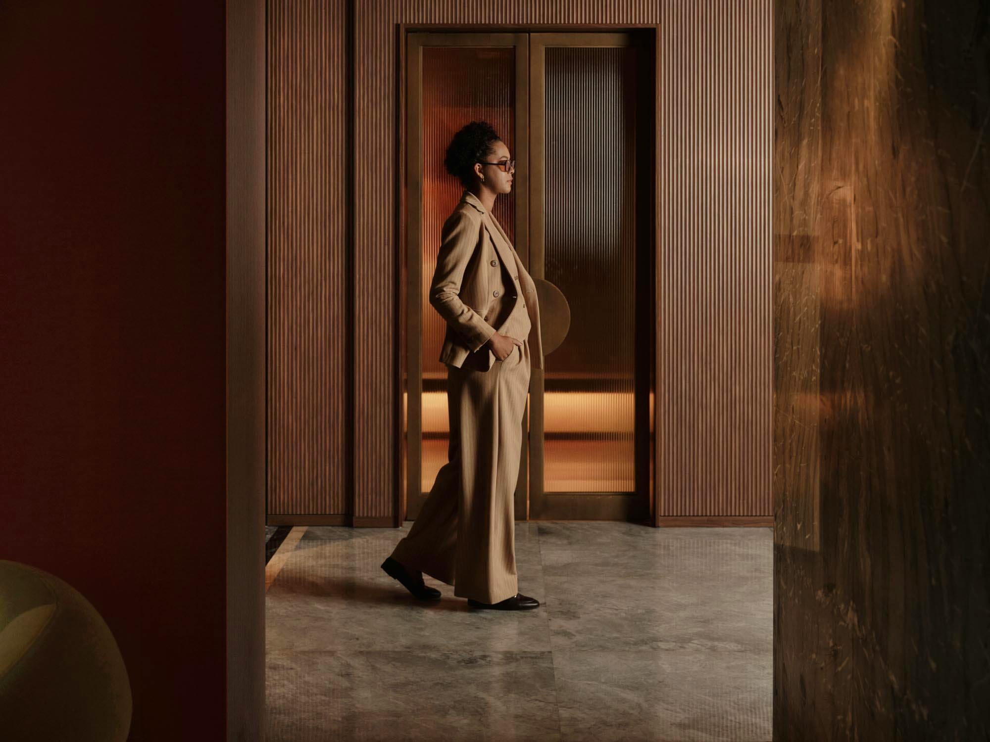 Woman in a tan suit crossing the marble lobby past tall fluted-glass doors